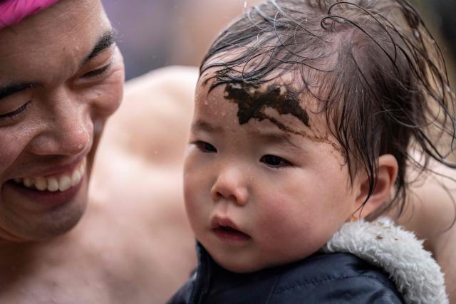 Mud is applied on a baby's forehead to pray for healthy growth during the Warabi Hadaka festival in Yotsukaido, Chiba Prefecture on February 25, 2026. (Photo by Yuichi YAMAZAKI / AFP)