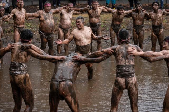 Participants form a circle in a muddy field at the end of the Warabi Hadaka festival in Yotsukaido, Chiba Prefecture on February 25, 2026. (Photo by Yuichi YAMAZAKI / AFP)