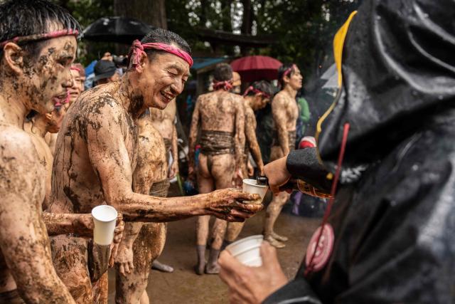 A participant receives a pour of sake by a bonfire after taking part in a horseback-style battle in a muddy field during the Warabi Hadaka festival at Mimusubi shrine in Yotsukaido, Chiba Prefecture on February 25, 2026. (Photo by Yuichi YAMAZAKI / AFP)
