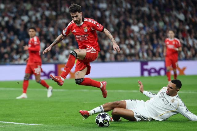 SL Benfica's Portuguese midfielder #27 Rafa Silva jumps over Real Madrid's English defender #12 Trent Alexander-Arnold during the UEFA Champions League knockout round play-off second leg football match between Real Madrid CF and SL Benfica at Santiago Bernabeu Stadium in Madrid on February 25, 2026. (Photo by Thomas COEX / AFP)