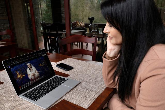 Albanian actress Anila Bisha looks at a screen during an AFP interview in Tirana on February 19, 2026 following the creation of AI-generated chatbot named "Diella", using her likeness and voice, delivered a speech in parliament without her knowledge. Over a 30-year career, Albanian actor Anila Bisha became renowned for playing complex women on the stage and screen, but now she lives in the shadow of her 'AI-generated' clone and a performance she never gave. Last September, Albania's Prime Minister Edi Rama announced, with much fanfare, the appointment of what he claimed was the first AI-generated minister, tasked with preventing corruption in public tenders. Within days, 'the minister' would deliver its inaugural parliamentary speech. (Photo by Adnan Beci / AFP)