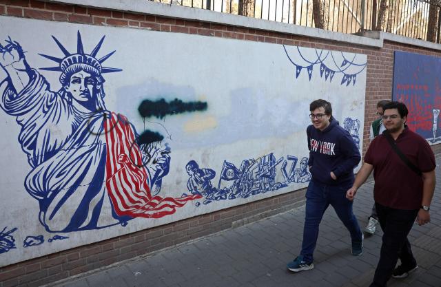 Iranians walk past an anti-US mural next to former US embassy in Tehran on February 26, 2026. A third round of indirect talks between the United States and Iran, mediated by Oman's foreign minister, opened in Geneva on February 26 morning, a diplomatic source told AFP. (Photo by AFP)