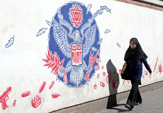 An Iranian woman walks past an anti-US wall mural next to the former US embassy in Tehran on February 26, 2026. A third round of indirect talks between the United States and Iran, mediated by Oman's foreign minister, opened in Geneva on February 26 morning, a diplomatic source told AFP. (Photo by AFP)