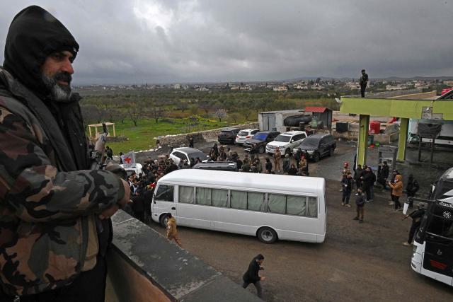 Security personnel and officials gather next to a bus with prisoners on board during an exchange of prisoners' ceremony between Syrian authorities and Druze fighters, on the outskirts of Suwaydah on February 26, 2026. (Photo by LOUAI BESHARA / AFP)