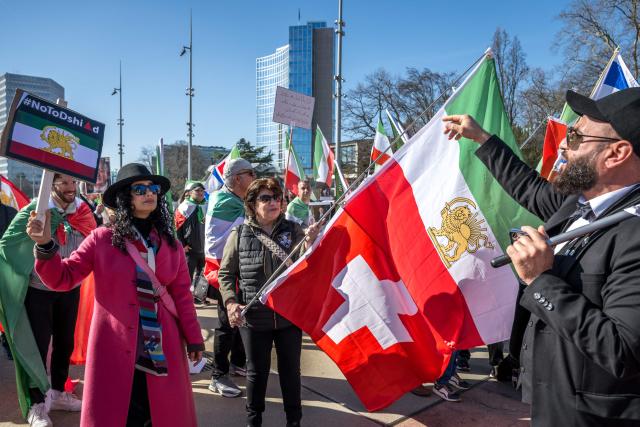 Protestors hold placards and wave flags during a demonstration organised by members of the Iranian diaspora outside the United Nations offices during new round of talks between the United States and Iran on Iran’s nuclear program, in Geneva on February 26, 2026. (Photo by Fabrice COFFRINI / AFP)