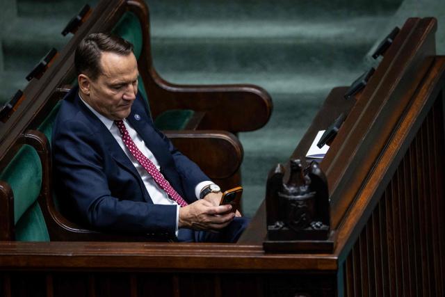 Poland's Minister of Foreign Afairs Radoslaw Sikorski holds his mobile phone and listens to a parliament member's question after he presented the main points of the Polish government's foreign policy to delegates of the Polish Parliament in Warsaw on February 26, 2026. (Photo by Wojtek RADWANSKI / AFP)