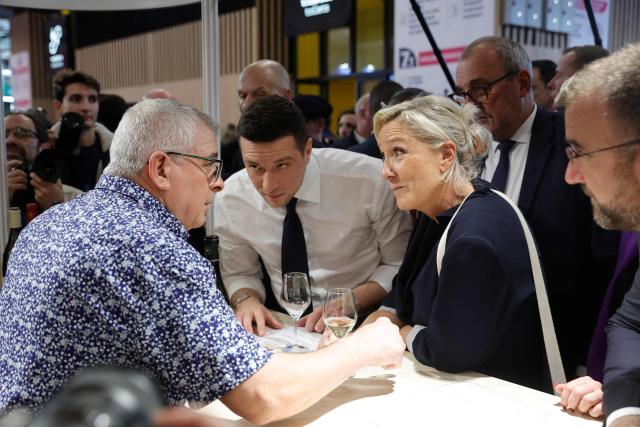President of French far-right party Rassemblement National (RN) Jordan Bardella (L) and  President of Rassemblement National parliamentary group Marine Le Pen speak with an exhibitor at a wine stand during their visit to the Paris International Agricultural Show (Salon de l'Agriculture) at Paris Expo Porte de Versailles in Paris on February 26, 2026. (Photo by GEOFFROY VAN DER HASSELT / AFP)