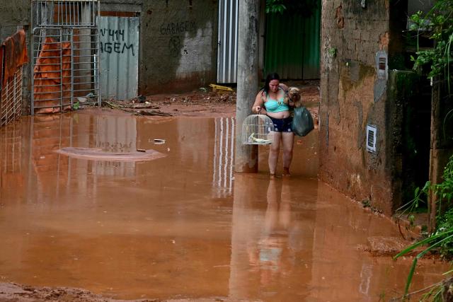 A residents rescues her pets after flooding and landslides in the Los Tres Molinos neighborhood in Juiz de Fora, Minas Gerais state, Brazil, on February 26, 2026. Despair hung over two cities in southeastern Brazil on February 25 as rescuers and residents searched for 21 people missing after torrential rains unleashed flooding and landslides that killed at least 46. (Photo by Pablo PORCIUNCULA / AFP)