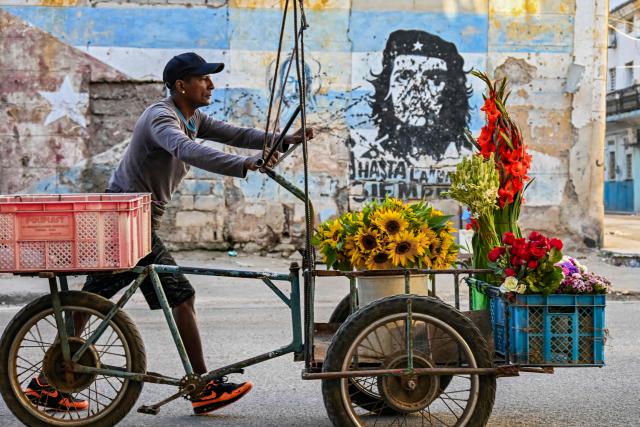 TOPSHOT - A flower street vendor pushes his cart past a mural depicting Argentine-born revolutionary leader Ernesto “Che” Guevara reading “Until victory, always.” in Havana on February 25, 2026. The US-imposed oil blockade on Cuba is upending the lives of everyday workers, who are switching jobs and ditching their cars to make do amid rolling blackouts and fuel shortages. (Photo by YAMIL LAGE / AFP)