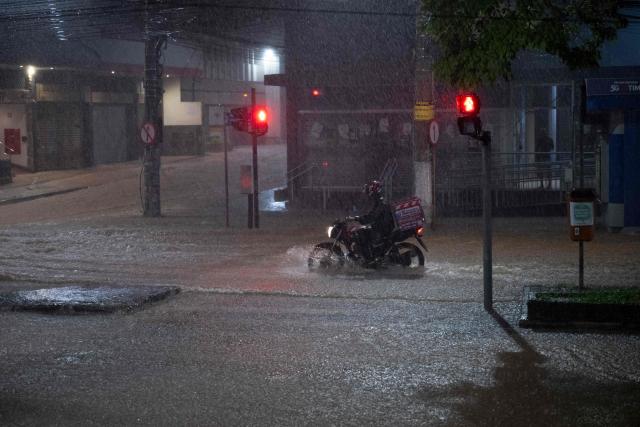 TOPSHOT - A delivery worker rides a motorbike on a flooded street during heavy rain in Juiz de Fora, Minas Gerais state, Brazil on February 25, 2026. The Civil Defense issued a mobile phone alert at 7 p.m. warning of a risk of landslides, flooding and inundation in the Democrata neighborhood, urging residents to evacuate and seek a safe location. (Photo by Pablo PORCIUNCULA / AFP)