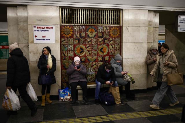 People take shelter during an air raid alert as other commuters pass by at a metro station in Kyiv on February 26, 2026, amid the Russian invasion of Ukraine. (Photo by HENRY NICHOLLS / AFP)