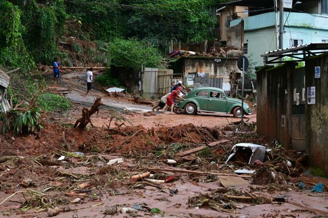 TOPSHOT - Residents push a Volkswagen Beetle after flooding and landslides in Tres Moinhos neighborhood in Juiz de Fora, Minas Gerais state, Brazil, on February 26, 2026. Despair hung over two cities in southeastern Brazil on February 25 as rescuers and residents searched for 21 people missing after torrential rains unleashed flooding and landslides that killed at least 46. (Photo by Pablo PORCIUNCULA / AFP)