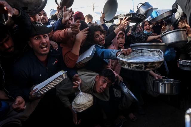 TOPSHOT - Palestinians react as they wait to receive food at a soup kitchen in Khan Yunis, in the southern Gaza Strip, on February 26, 2026. Despite a US-brokered ceasefire that entered its second phase last month, shortages remain in Gaza, whose battered economy and material damage have rendered most residents at least partly dependent on humanitarian aid for their basic needs. (Photo by BASHAR TALEB / AFP)