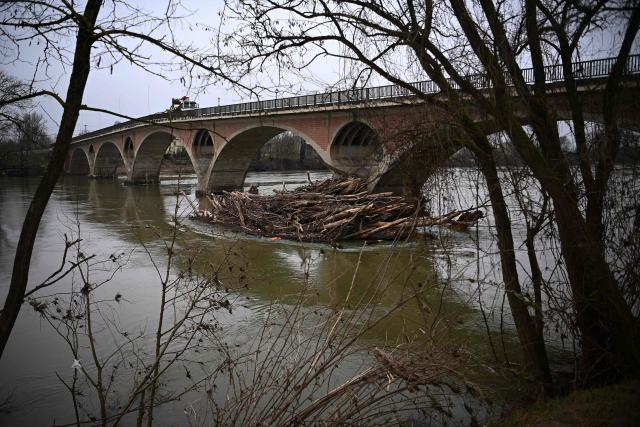 This photograph shows tree trunks stuck by a bridge days after Storm Nils hit the area along the River Garonne at Tonneins, south-western France on February 26, 2026. The record streak of consecutive rainy days in France ended on February 23, at 40 days, but the flooding is still not over despite signs of improvement, according to Météo-France. A new record was also set for the length of time France has been under red flood alert, Vigicrues reported on February 24, with 14 days. In the West, water levels continued to slowly recede, suggesting a gradual return to normal for some affected areas. (Photo by Christophe ARCHAMBAULT / AFP)