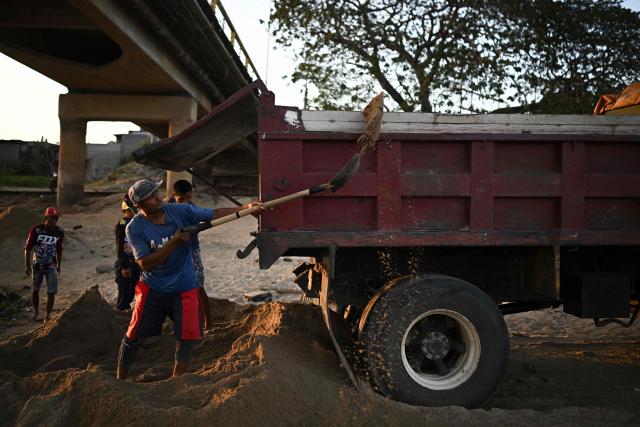 Men shovel sand into trucks at the Maria Nieves bridge on the banks of the Apure River in San Fernando de Apure, Apure State, Venezuela, on February 26, 2026. (Photo by Federico PARRA / AFP)