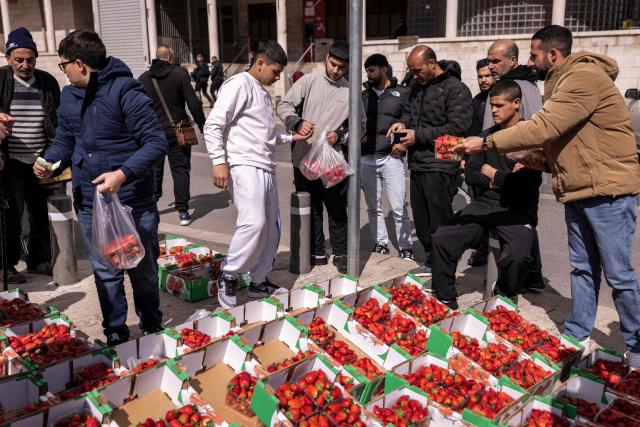 People buy strawberries from a produce vendor after the second Friday noon prayers of the holy month of Ramadan in the old city of Jerusalem on February 27, 2026. Muslims throughout the world are marking the month of Ramadan, the holiest month in the Islamic calendar, during which devotees fast from dawn until dusk. (Photo by JOHN WESSELS / AFP)