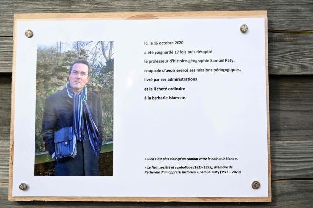 (FILES) This photograph shows a commemorative plaque  for slain teacher Samuel Paty (portrait) near the Bois d'Aulne school in Conflans-Sainte-Honorine, outside Paris on October 16, 2023. On February 27, 2026, the prosecution requested that the sentences of the two initiators of a hate campaign against Samuel Paty be increased to 20 years' imprisonment on appeal. The campaign was launched before his beheading by a Chechen jihadist for showing caricatures of the Prophet during a lesson on freedom of expression. (Photo by Bertrand GUAY / POOL / AFP)