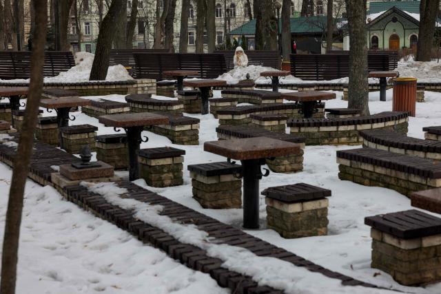 A woman sits on a park bench near tables and snowy grounds in Kyiv on February 27, 2026, amid the Russian invasion of Ukraine. (Photo by Tetiana DZHAFAROVA / AFP)