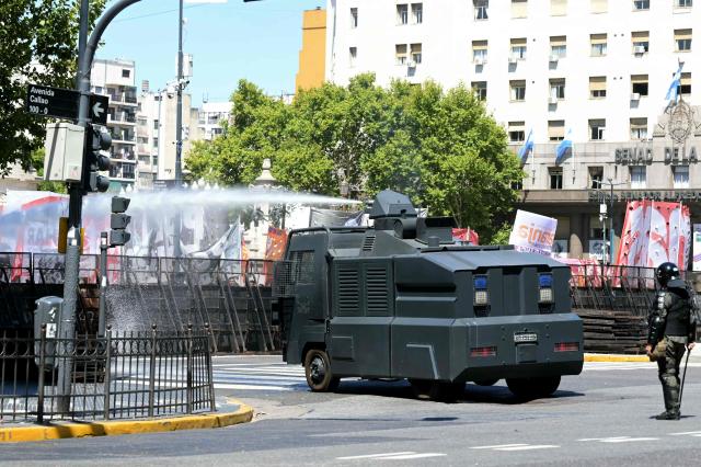 A Gendarmerie water canon shoots water to disperse people protesting outside the Congress building, where Argentina's President Javier Milei's labour reforms are being treated, in Buenos Aires on February 27, 2026. The reforms pushed by budget-cutting Milei would ease hiring and firing, reduce severance pay, limit the right to strike, extend work hours and restrict holidays. Approved by the Chamber of Deputies on February 20, the package is being debated in the Senate on February 27 for a final green light. (Photo by Juan Mabromata / AFP)