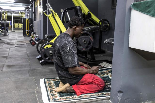 Doudou Sene prays after breaking his fast at a gym during the holy month of Ramadan in Dakar, on February 23, 2026. What started as small workouts in one of the many outdoor gyms that proliferate in Dakar slowly turned into a passion for Doudou Sene. People kept telling him that he had potential in the world of fitness, and in 2019 he began to train seriously. In 2021, he participated in his first powerlifting competition in Dakar and finished first in the under?83 kg category. Soon after, he traveled to The Gambia for another competition, where he finished third. After succeeding as a powerlifter, he decided to switch to bodybuilding, a little?known sport in Senegal with few role models, such as Sidy Pouye, who has managed to build a successful career abroad as a bodybuilder. People dont know much about the sport, but that doesnt stop Doudou from following his passion. During the holy month of Ramadan, training and maintaining a proper diet become challenging. Doudou normally eats five to six meals a day to maintain his gains, but during Ramadan this is reduced to two or three. He prefers to train at the gym where he works right before breaking the fast, and then stays late to help clients with their workouts. Family and religion are his driving forces as he continues pushing himself, even during Ramadan, to achieve his goal of making a living as a bodybuilder and providing for his family. (Photo by PATRICK MEINHARDT / AFP)
