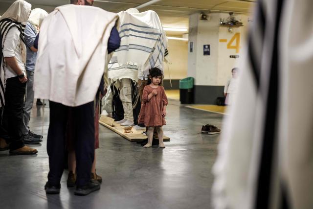 A girl watches as Jews pray as they take shelter in Tel Aviv on February 28, 2026. The Israeli military said its strikes on Iran, in coordination with the United States, targeted dozens of military sites and followed months of joint planning between the allies. (Photo by Jack GUEZ / AFP)