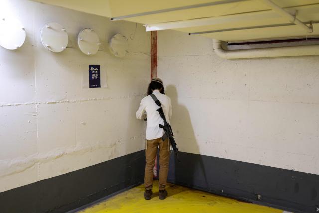 TOPSHOT - An armed Jewish man prays as people take shelter in Tel Aviv on February 28, 2026. The Israeli military said its strikes on Iran, in coordination with the United States, targeted dozens of military sites and followed months of joint planning between the allies. (Photo by ilia YEFIMOVICH / AFP)