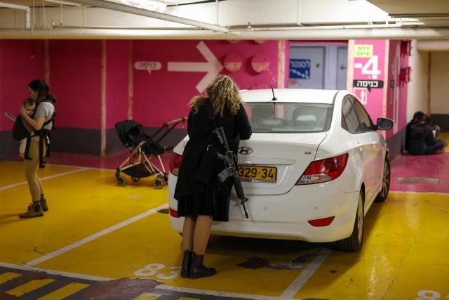 TOPSHOT - People take shelter in an underground garage in Tel Aviv on February 28, 2026. The United States and Israel launched a wave of strikes against targets in Iranian cities on February 28, triggering explosions and columns of smoke in the capital Tehran. Iran responded by launching retaliatory missile attacks, according to the Israeli military, as US diplomats in the Gulf and Israeli civilians were ordered to seek shelter. (Photo by Ilia YEFIMOVICH / AFP)