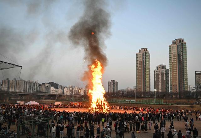 People gather around a huge bonfire during an event to celebrate the upcoming 'Jeongwol Daeboreum', a festival celebrating the first full moon of the Lunar New Year, at a riverside park in Seoul on February 28, 2026. (Photo by Jung Yeon-je / AFP)