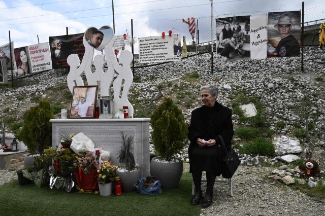 An elderly woman sits next to a victim memorial at the crash site of the Tempi railway collision, marking three years since the country's worst rail tragedy, in the valley of Tempi, near Larissa, on February 28, 2026. Thousands of people across Greece will demonstrate on February 28, 2026, in solidarity with victims of the country's worst train tragedy, which claimed 57 lives in 2023 and rattled the government of Prime Minister Kyriakos Mitsotakis. (Photo by SAKIS MITROLIDIS / AFP)