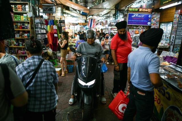 A motorist ride his motorbike as visitors walk through an alley at Sampheng Market in Bangkok on February 28, 2026. (Photo by Amaury PAUL / AFP)