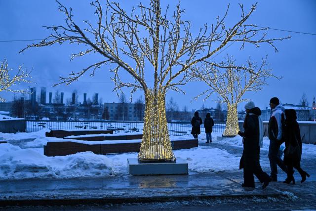 People walk on a street next to Zaryadye Park at dusk in central Moscow on February 28, 2026. (Photo by HECTOR RETAMAL / AFP)