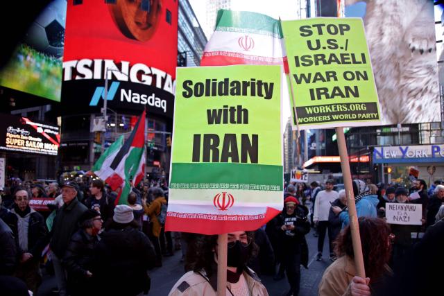 People hoist signs during a "Stop the War on Iran" protest in Times Square in New York City on February 28, 2026. The US and Israel launched an attack of unprecedented scale against Iran earlier on Saturday. (Photo by Leonardo MUNOZ / AFP)
