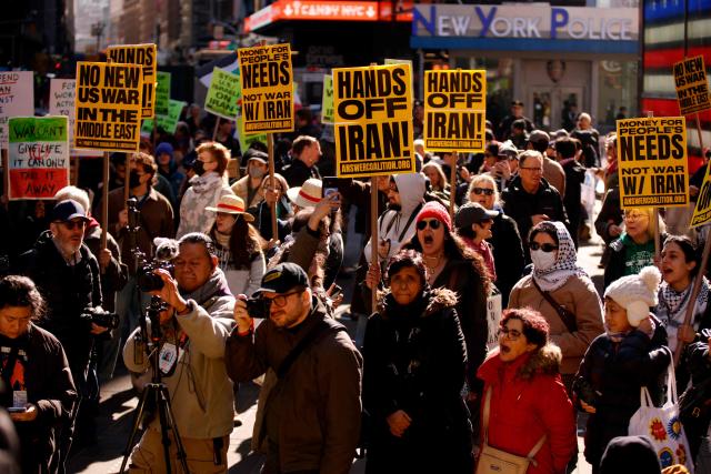 People hoist signs during a "Stop the War on Iran" protest in Times Square in New York City on February 28, 2026. The US and Israel launched an attack of unprecedented scale against Iran earlier on Saturday. (Photo by Leonardo MUNOZ / AFP)