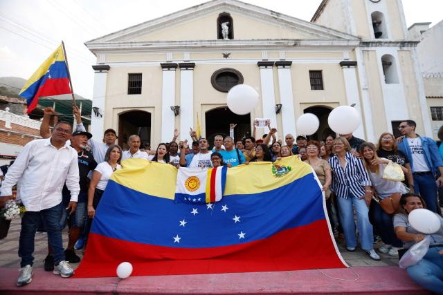 Former political prisoners, their relatives and friends hold a Venezuelan flag and chant slogans outside the church after a Mass for freedom in Maiquetia, La Guaira State, Venezuela, on February 28, 2026. (Photo by Pedro MATTEY / AFP)