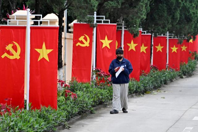 A woman uses her phone next to Vietnamese national flags Communist Party of Vietnam flags in Hanoi on February 27, 2026. Vietnam's new artificial intelligence law went into effect on March 1, making the country the first in Southeast Asia with a comprehensive framework to regulate the fast-evolving technology. (Photo by Nhac NGUYEN / AFP) / To go with 'VIETNAM-AI-LAW' by Tran Thi Minh Ha