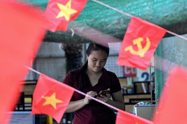 A girl uses her phone next to Vietnamese national flags Communist Party of Vietnam flags in Hanoi on February 27, 2026. Vietnam's new artificial intelligence law went into effect on March 1, making the country the first in Southeast Asia with a comprehensive framework to regulate the fast-evolving technology. (Photo by Nhac NGUYEN / AFP) / To go with 'VIETNAM-AI-LAW' by Tran Thi Minh Ha