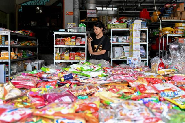 A shopkeeper uses her phone while waiting for customers at a grocery store in Hanoi on February 27, 2026. Vietnam's new artificial intelligence law went into effect on March 1, making the country the first in Southeast Asia with a comprehensive framework to regulate the fast-evolving technology. (Photo by Nhac NGUYEN / AFP) / To go with 'VIETNAM-AI-LAW' by Tran Thi Minh Ha
