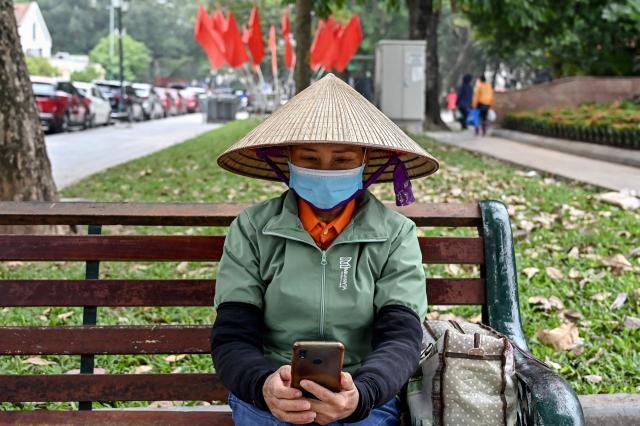 (FILES) A worker uses a mobile phone at a park in Hanoi on December 18, 2023. Vietnam's new artificial intelligence law went into effect on March 1, 2026, making the country the first in Southeast Asia with a comprehensive framework to regulate the fast-evolving technology. (Photo by Nhac NGUYEN / AFP) / To go with 'VIETNAM-AI-LAW' by Tran Thi Minh Ha
