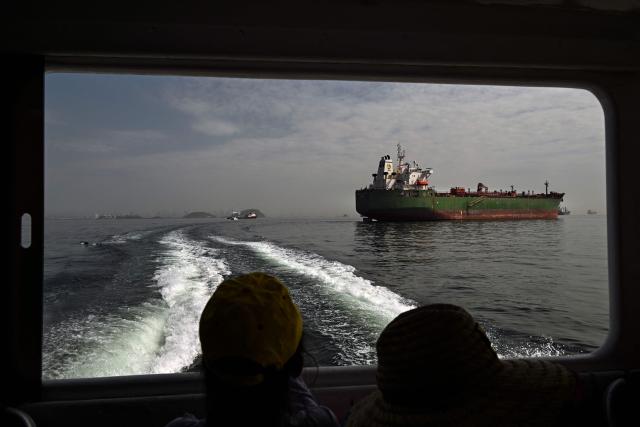 Tourists look at a cargo ship waiting to enter the Panama Canal in Panama City on February 28, 2026. (Photo by MARTIN BERNETTI / AFP)