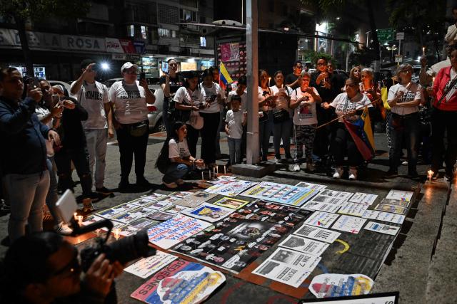 People hold candles during a vigil to demand the release of political prisoners outside of Helicoide prision in Caracas on February 28, 2026. More than 500 political prisoners have been released as part of a liberation process promoted by interim president Delcy Rodriguez, who assumed power after the capture of Nicolas Maduro in a US military operation. (Photo by Juan BARRETO / AFP)