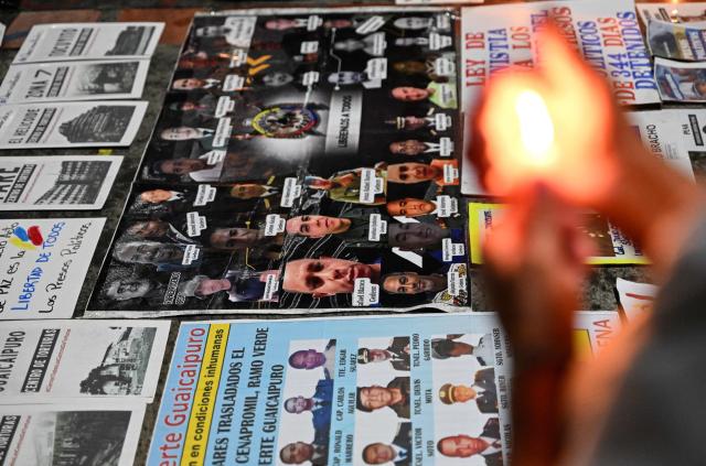 A woman holds a candle next to the pictures of political prisoners to demand their release outside of Helicoide prision in Caracas on February 28, 2026. More than 500 political prisoners have been released as part of a liberation process promoted by interim president Delcy Rodriguez, who assumed power after the capture of Nicolas Maduro in a US military operation. (Photo by Juan BARRETO / AFP)