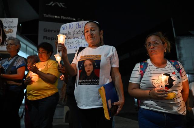 People hold candles during a vigil to demand the release of political prisoners outside of Helicoide prision in Caracas on February 28, 2026. More than 500 political prisoners have been released as part of a liberation process promoted by interim president Delcy Rodriguez, who assumed power after the capture of Nicolas Maduro in a US military operation. (Photo by Juan BARRETO / AFP)