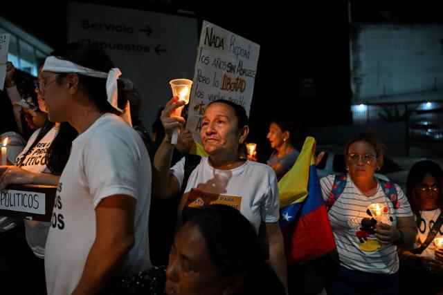 People hold candles during a vigil to demand the release of political prisoners outside of Helicoide prision in Caracas on February 28, 2026. More than 500 political prisoners have been released as part of a liberation process promoted by interim president Delcy Rodriguez, who assumed power after the capture of Nicolas Maduro in a US military operation. (Photo by Juan BARRETO / AFP)