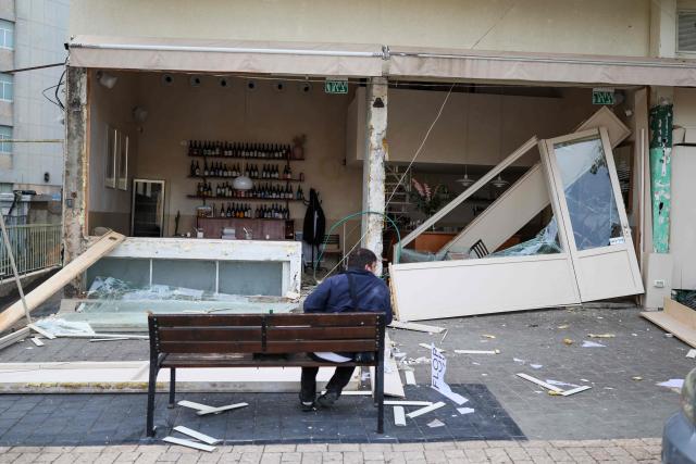A person sits in front of a store damaged in a reported overnight Iranian strike in Tel Aviv on March 1, 2026. US President Donald Trump said February 28 that Iran's supreme leader Ayatollah Ali Khamenei was dead, after Israel and the United States launched an attack of unprecedented scale aimed at bringing down the Islamic republic. (Photo by Ilia YEFIMOVICH / AFP)
