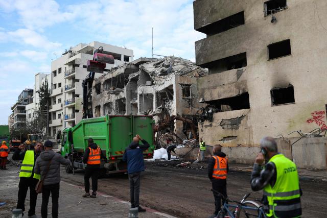TOPSHOT - People look at a building damaged in a reported overnight Iranian strike in Tel Aviv on March 1, 2026. US President Donald Trump said February 28 that Iran's supreme leader Ayatollah Ali Khamenei was dead, after Israel and the United States launched an attack of unprecedented scale aimed at bringing down the Islamic republic. (Photo by Ilia YEFIMOVICH / AFP)