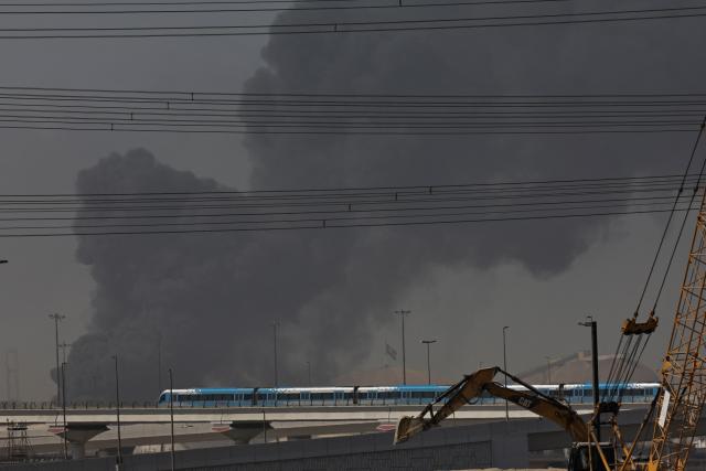 A metro train passes by a plume of smoke rising from the port of Jebel Ali following a reported Iranian strike in Dubai on March 1, 2026. Ayatollah Ali Khamenei, Iran's supreme leader since 1989 and sworn enemy of the West, was killed in the opening salvo of a massive US and Israeli attack, sparking a new wave of retaliatory missile strikes from Tehran on March 1. (Photo by Fadel SENNA / AFP)