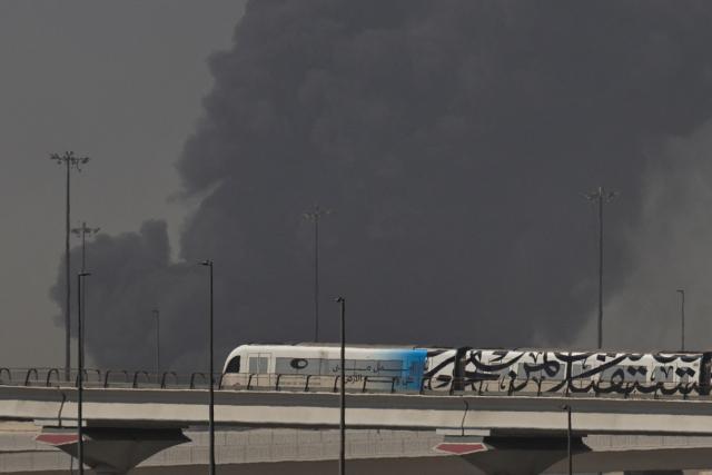 TOPSHOT - A metro train passes a plume of smoke rising from the port of Jebel Ali following a reported Iranian strike in Dubai on March 1, 2026. Ayatollah Ali Khamenei, Iran's supreme leader since 1989 and sworn enemy of the West, was killed in the opening salvo of a massive US and Israeli attack, sparking a new wave of retaliatory missile strikes from Tehran on March 1. (Photo by Fadel SENNA / AFP)