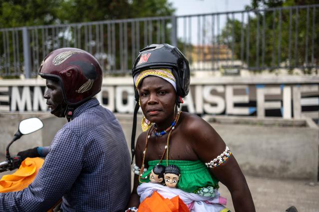 A woman rides on the back of a motorbike carrying a statuette of twins tied around her waist in Lome on February 28, 2026. (Photo by OLYMPIA DE MAISMONT / AFP)