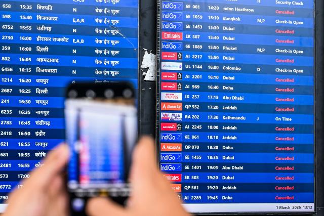 A passenger takes pictures of a flight information board at the Chhatrapati Shivaji Maharaj International Airport in Mumbai on March 1, 2026 after India's two largest private carriers IndiGo and Air India suspended flights to all destinations in the Middle East. Thousands of flights have been delayed or cancelled in the biggest disruption to global air transport since the Covid pandemic as airlines suspend services to the Middle East following the US and Israeli attacks on Iran. (Photo by Punit PARANJPE / AFP)