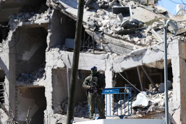 TOPSHOT - An Israeli soldier guards an area in front of a destroyed building that was hit by a reported overnight Iranian strike in Tel Aviv on March 1, 2026. Ayatollah Ali Khamenei, Iran's supreme leader since 1989 and sworn enemy of the West, was killed in the opening salvo of a massive US and Israeli attack, sparking a new wave of retaliatory missile strikes from Tehran on March 1. (Photo by Ilia YEFIMOVICH / AFP)